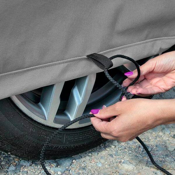 Person securing a car cover with rope around tire for added stability and protection.